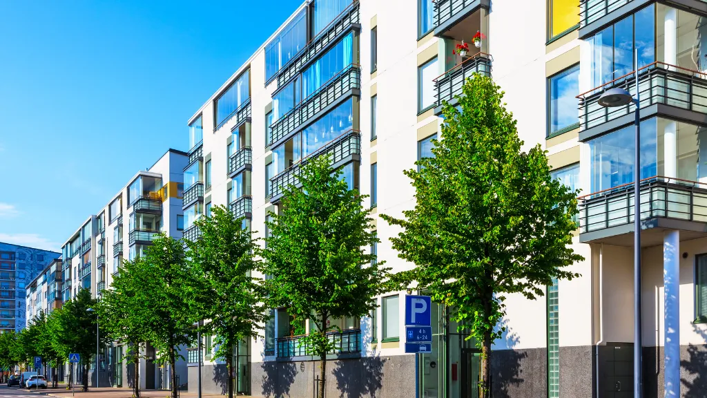 A modern mid-rise apartment building lined with trees along a city street, showcasing contemporary multifamily residential development. The image represents urban housing, rental properties, and real estate investment opportunities, making it ideal for topics such as **real estate terms every investor should know**, multifamily investing, apartment buildings, residential property management, cash flow, appreciation, cap rates, and commercial real estate fundamentals.