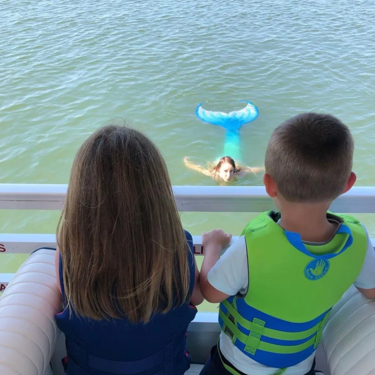 two children looking at mermaid in water