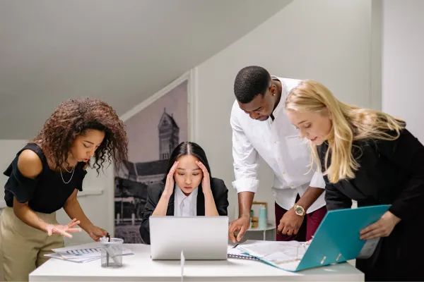 Team gathered around a laptop looking stressed while trying to solve a problem together.