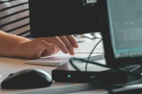 Close-up of hands typing on a white keyboard with a computer mouse and monitor in soft focus.