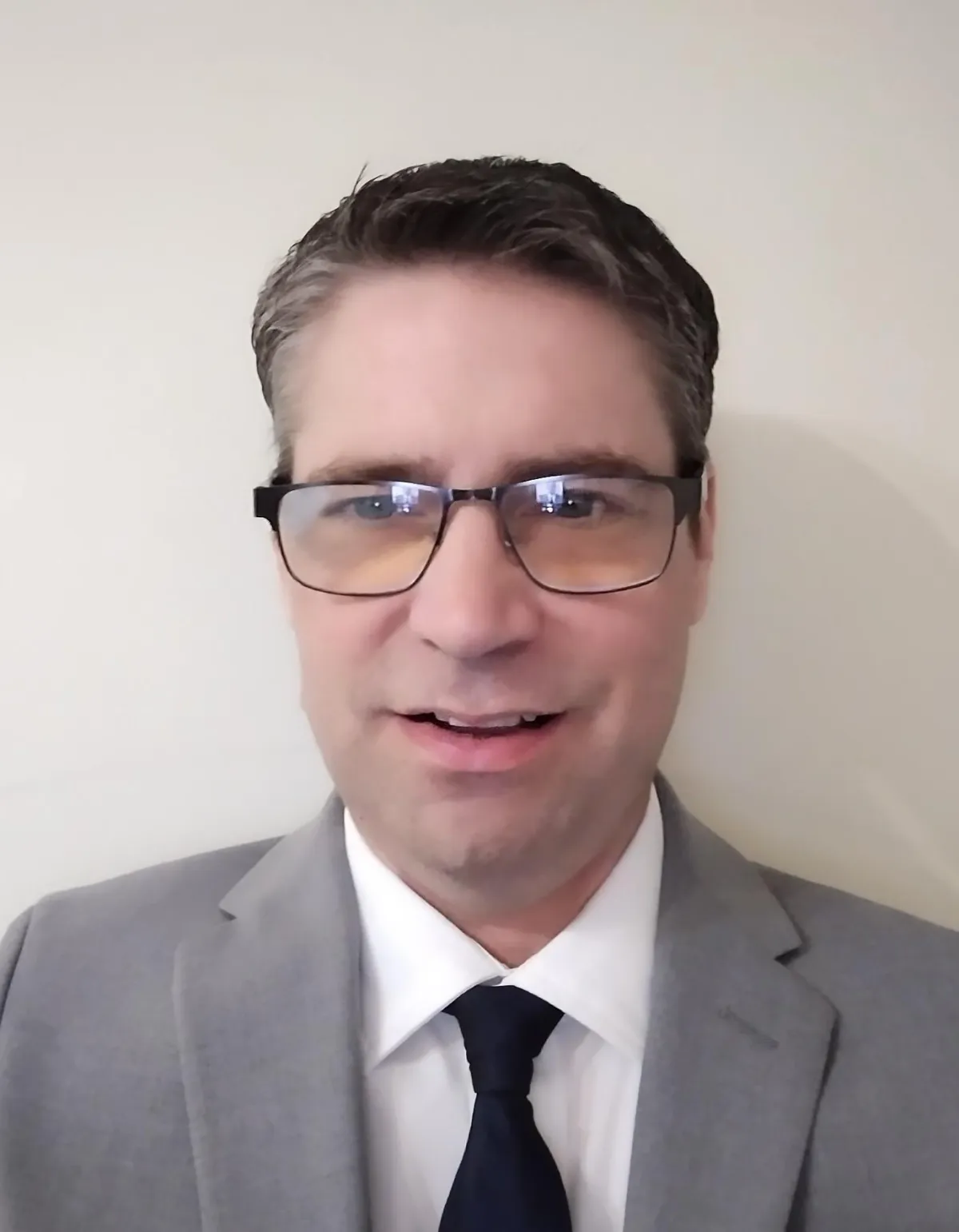 A friendly male financial advisor in his 40s, smiling and answering a phone call at a bright office desk with a notepad and pen, cityscape visible through the window. 3:2 aspect ratio, professional, approachable.