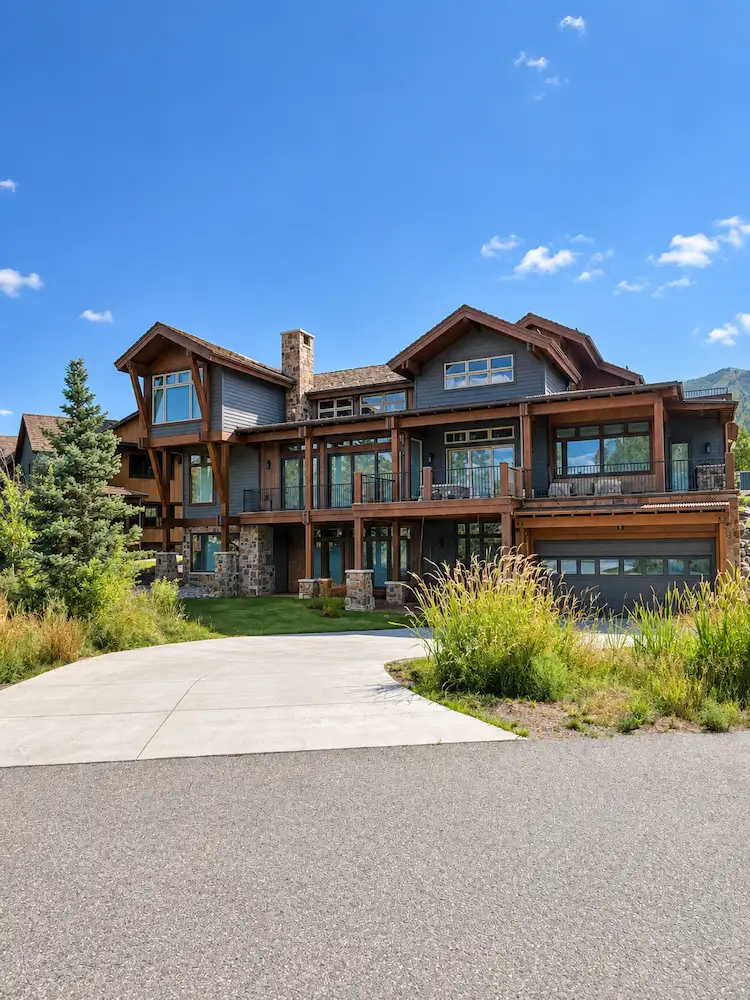 Large three-storey mountain lodge-style house with dark siding, wood trim, stone chimney and balconies