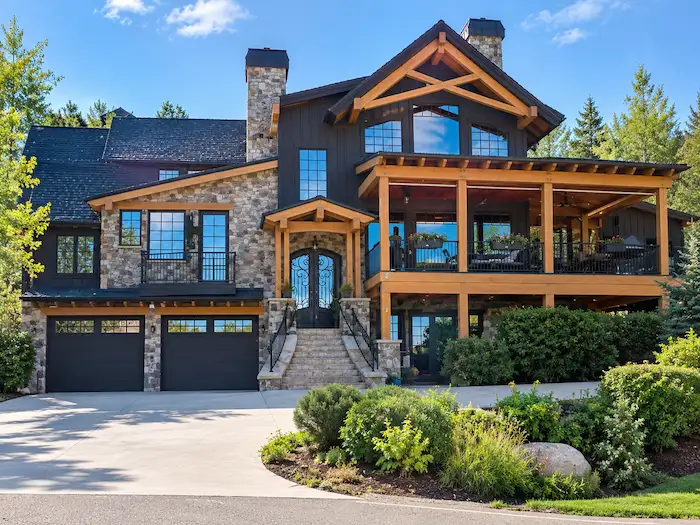 Two-storey home with black siding, stone walls, timber-framed gables, covered deck, arched front doors and double garage