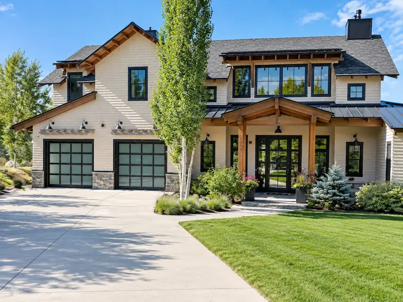 Green two-storey house with cedar shake gable, arched window, wooden deck and front stairs surrounded by evergreen trees
