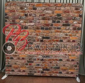 Rustic brick wall photo booth backdrop – textured red-brown and orange distressed brick pattern covering the full panel, standing on floor with gray curtain behind, perfect for industrial, urban, vintage, wedding, or modern event setups