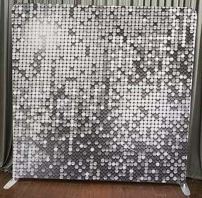 Silver sequin photo booth backdrop – shimmering metallic disc tiles in cool silver tones with sparkling light reflections, standing on floor with gray curtain behind, ideal for glamorous, modern, wedding, corporate, or high-energy party events