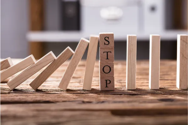 Wooden blocks spelling out the word STOP stand in a line, with dominoes falling on the left side.