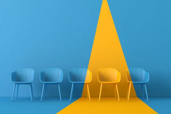 Four light blue chairs are lined up against a blue wall, with a bright yellow spotlight illuminating the two chairs on the right.