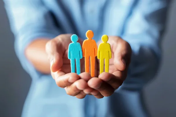 A person holds three small, colorful figures representing people in their cupped hands.