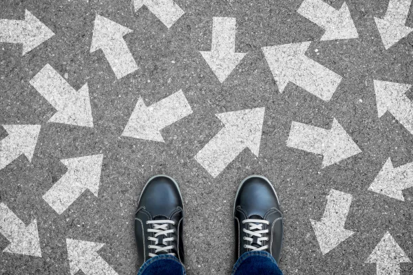 Pair of dark lace-up shoes standing on a gray pavement covered with scattered white arrows pointing in different directions.