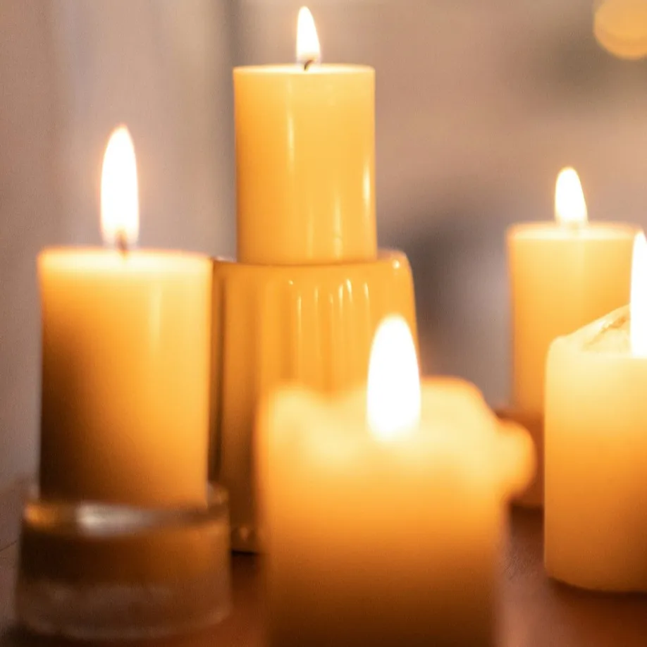 A serene arrangement of softly glowing candles, creating a warm and peaceful ambiance. The candles are placed at different heights, casting a gentle light that enhances the calm and meditative atmosphere.