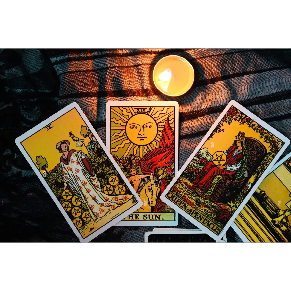 A display of three tarot cards laid out on a dark cloth, featuring "Nine of Pentacles," "The Sun," and "Queen of Pentacles." A lit candle casts a warm glow over the cards, adding a mystical ambiance to the scene. The cards represent themes of success, joy, and nurturing energy, often used in tarot readings for insight and guidance.