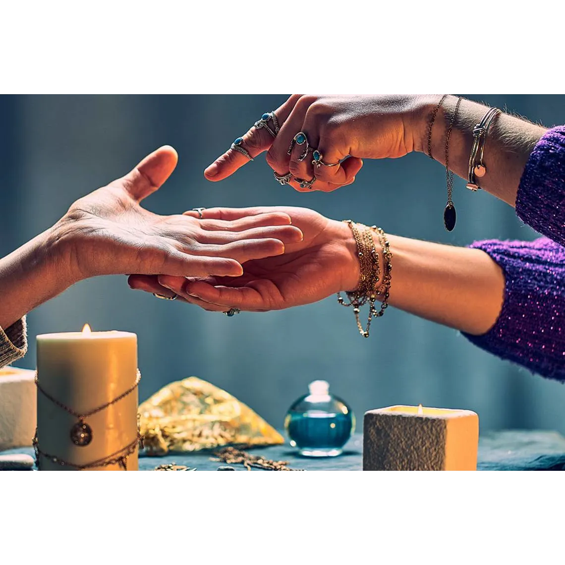 A close-up of a palm reading session, with one hand gently holding the other while a finger traces the lines of the palm. Both individuals are wearing multiple rings and bracelets, and the setting includes candles and spiritual objects, creating an intimate and mystical atmosphere. The image conveys the practice of palmistry and spiritual guidance.