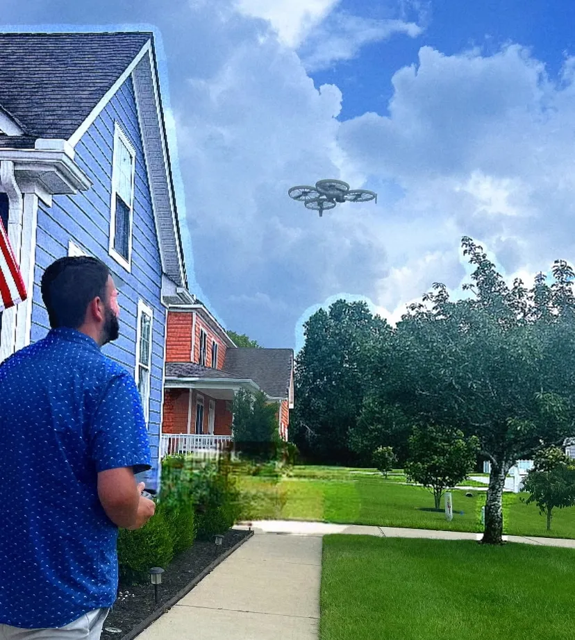 Man operating a drone outside a suburban home with blue siding, flying above a green lawn and trees under a partly cloudy sky.