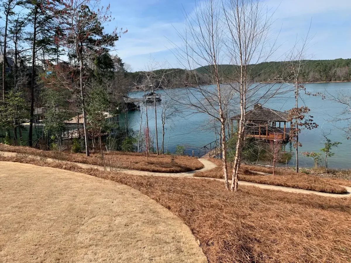 Alt Text: Stacks of pine straw bales near a semi-truck at an outdoor supply yard, ready for delivery.