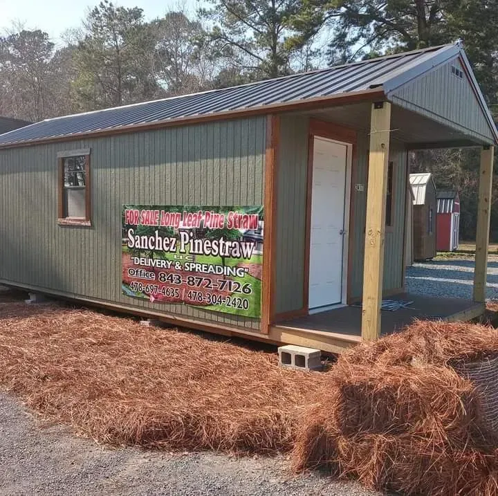 Stacks of pine straw bales arranged around a semi-truck trailer on a distribution yard, ready for delivery and installation.