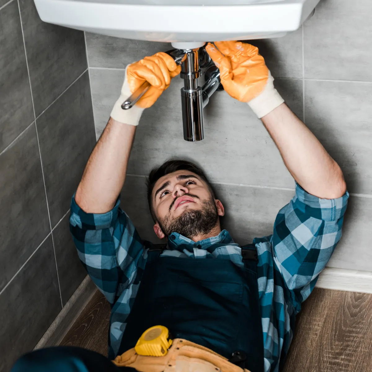 a repairman is underneath a sink tuning a wrench