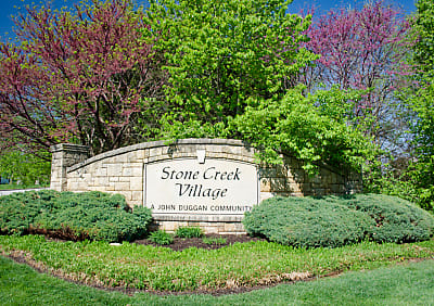 A stone entrance sign reading ‘Stone Creek Village’ surrounded by landscaping, shrubs, and colorful trees.