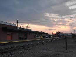 A railroad track running beside an industrial building during a cloudy sunset.