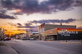 A small-town main street at sunset with shops, storefronts, and colorful clouds in the sky