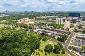 An aerial view of a suburban neighborhood surrounded by trees, with a city skyline visible in the distance.