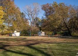 An open grassy park area with mature trees and a small white building in the distance.