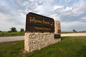 A stone entrance sign reading ‘Tallgrass Prairie National Preserve’ beside a road under a partly cloudy sky
