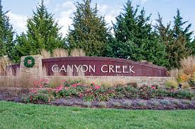 A brick entrance sign reading ‘Canyon Creek’ surrounded by landscaping, flowers, and evergreen trees.