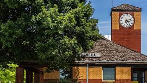 A historic brick building with a clock tower partially shaded by a large tree
