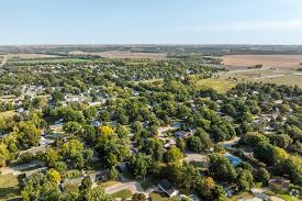An aerial view of a suburban neighborhood surrounded by trees and fields stretching into the distance