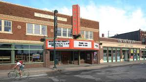 A historic brick theater and storefronts along a downtown street, with a bicycle parked outside.