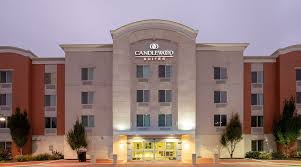 A lit-up hotel entrance at dusk with a modern multi-story facade and landscaped front walkway.