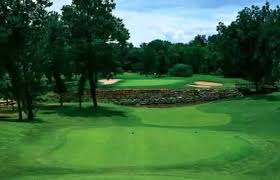 A green golf course fairway surrounded by trees with a sand trap and landscaped rock border near the green
