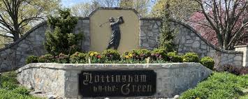 A stone entrance sign reading ‘Nottingham by the Green’ with a golfer silhouette, surrounded by shrubs and trees