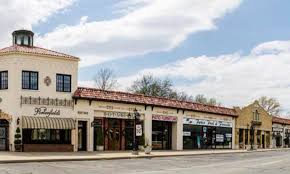 A row of shops and restaurants in a Mediterranean-style shopping district with a tower and tiled roof.