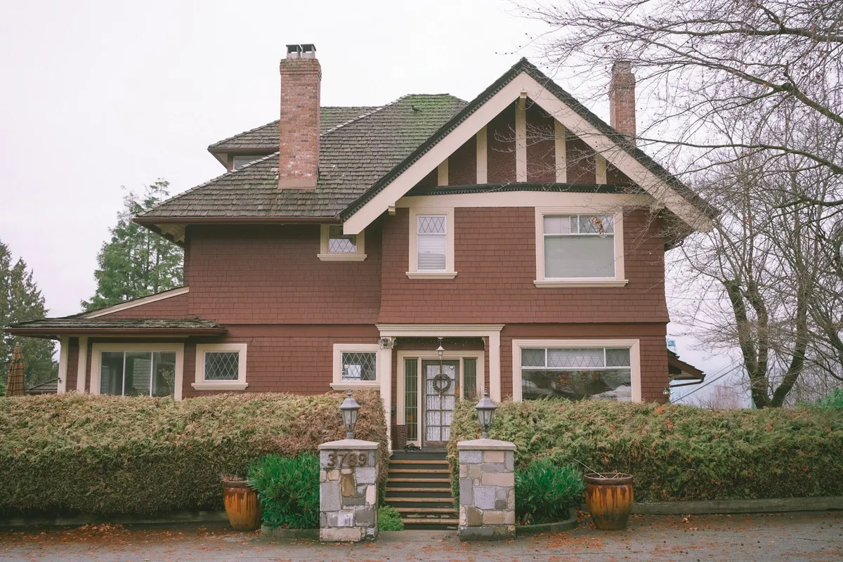 Two-story craftsman-style custom home in the Inland Northwest with a steep shingled roof, covered front porch, stone entry pillars, and mature landscaping
