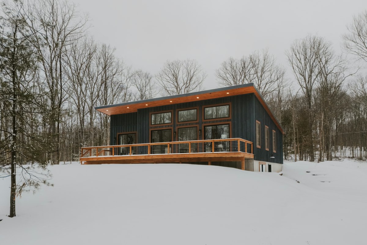 Modern custom home with dark siding and wood-accent deck on a snow-covered wooded Inland Northwest lot