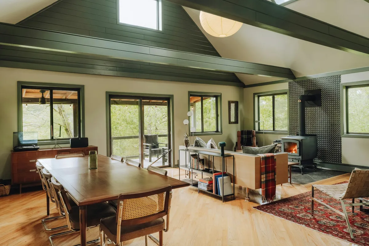 Warm, open-plan custom home living and dining room with hardwood floors, vaulted ceiling, and a wood stove on a winter day