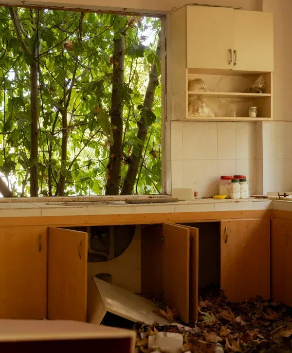A severely fire-damaged kitchen showing charred walls, appliances, a stovetop, and sink, with insulation hanging from the ceiling.