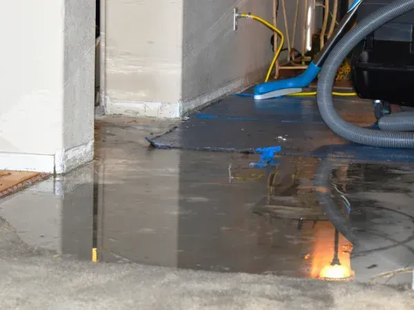 A water-damaged room with standing water on the floor, reflected light, and utility equipment. 