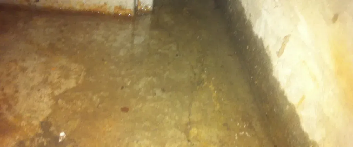 A concrete basement floor covered in standing water, showing signs of leakage and rust-colored stains.