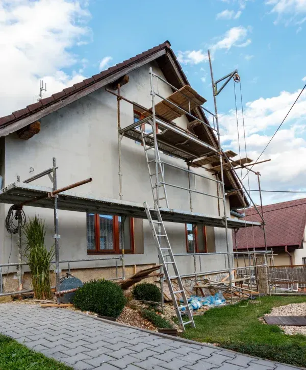A two-story house under renovation, covered partially with scaffolding and a ladder on a cloudy day.