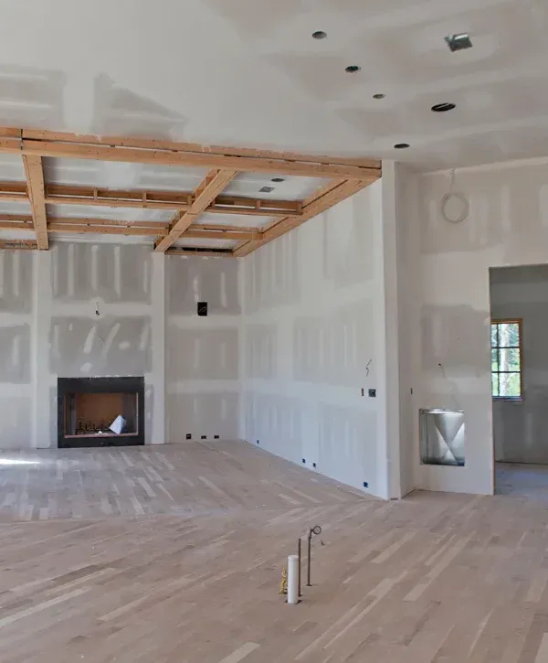 An unfinished living room with light hardwood floors, dry-walled white walls, and an open fireplace.