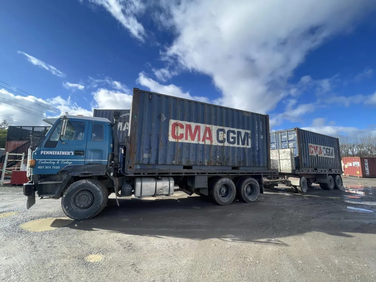 Pennefather’s truck transporting two CMA CGM shipping containers on a gravel yard under blue sky