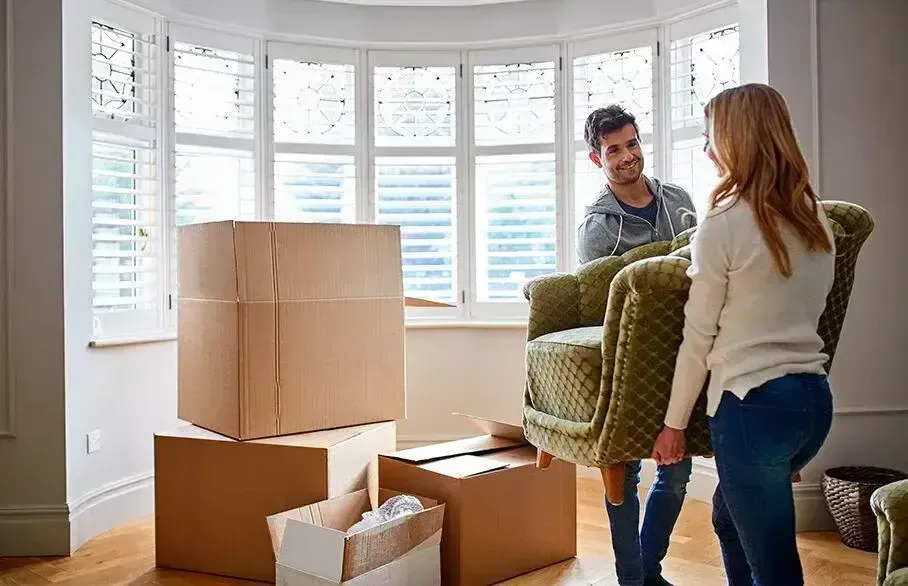 Couple moving a chair into their new Galveston apartment with large bay windows.