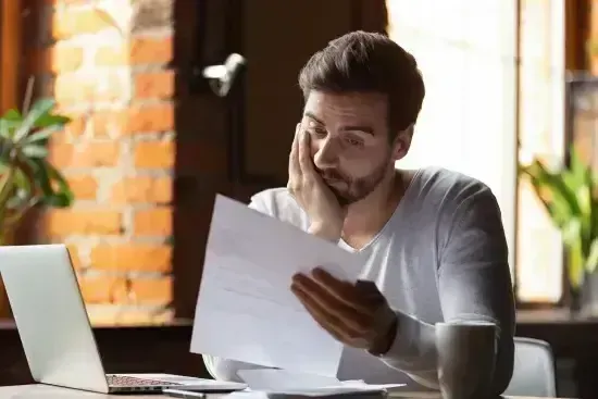 Concerned man reviewing rental documents on laptop at a cafe table.