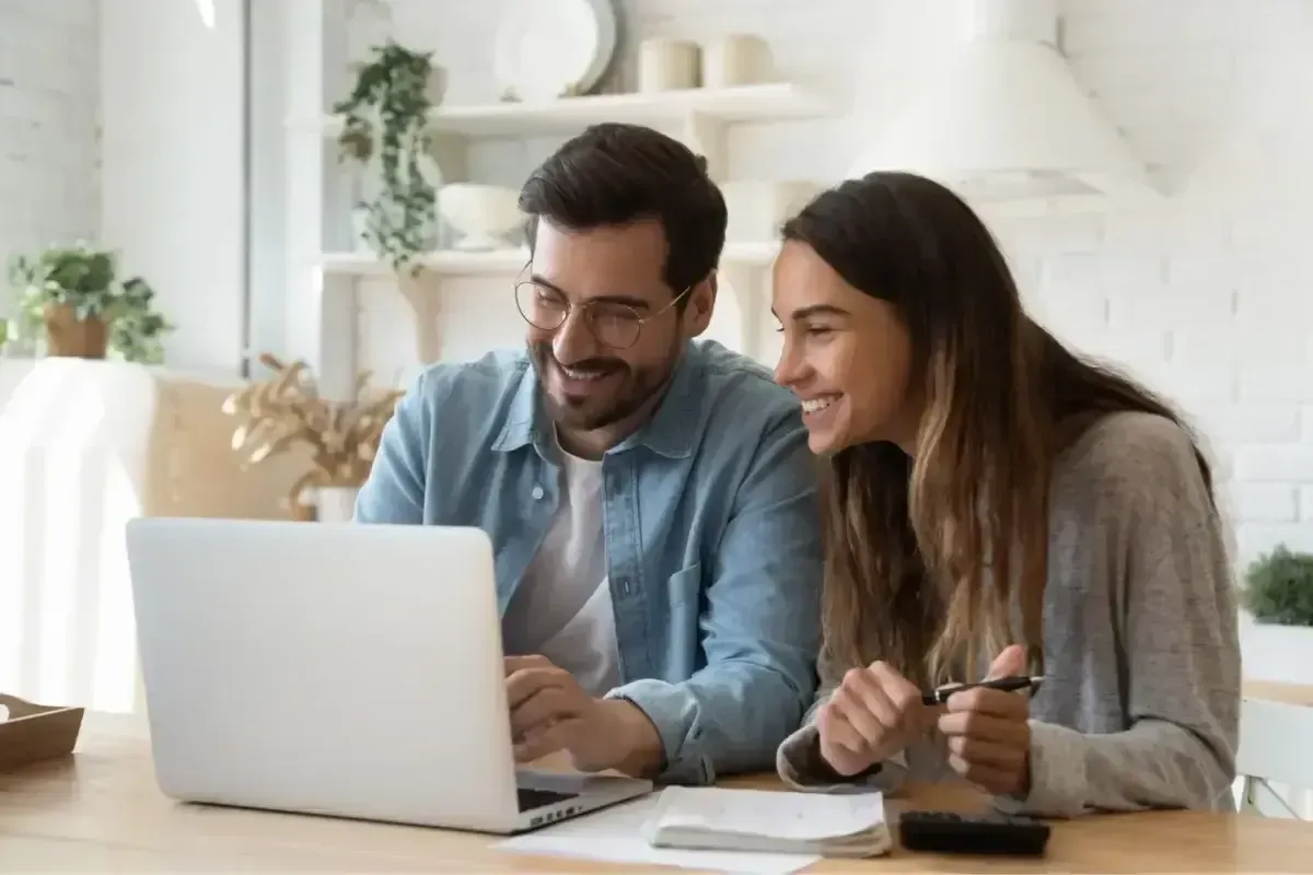 Smiling couple using laptop to search for Galveston apartments and calculate rent.