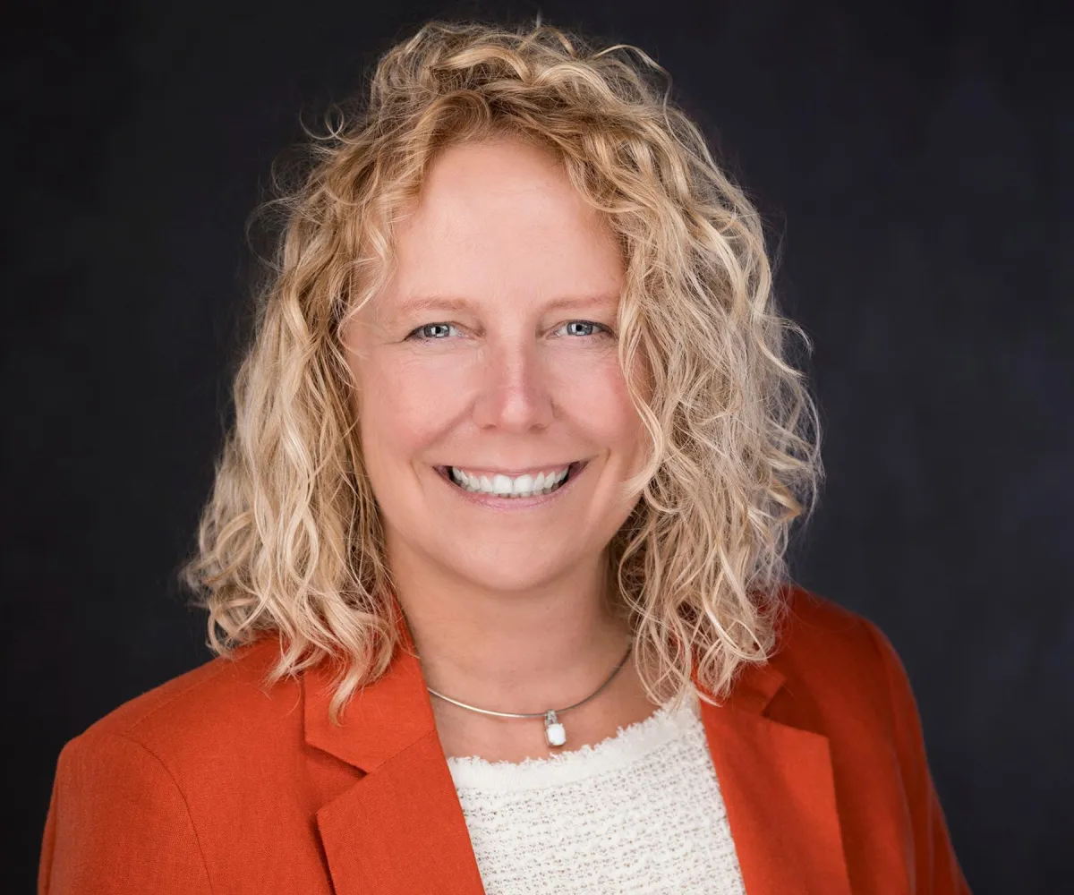 Professional headshot on light gray backdrop — confident smile, studio lighting