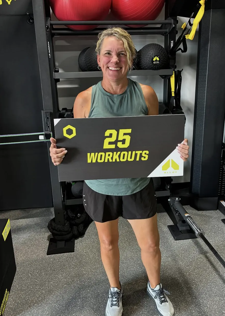 A proud member holding a sign marking 25 completed workouts at Alloy Personal Training, showcasing dedication and progress in a supportive fitness environment in Parker, CO.