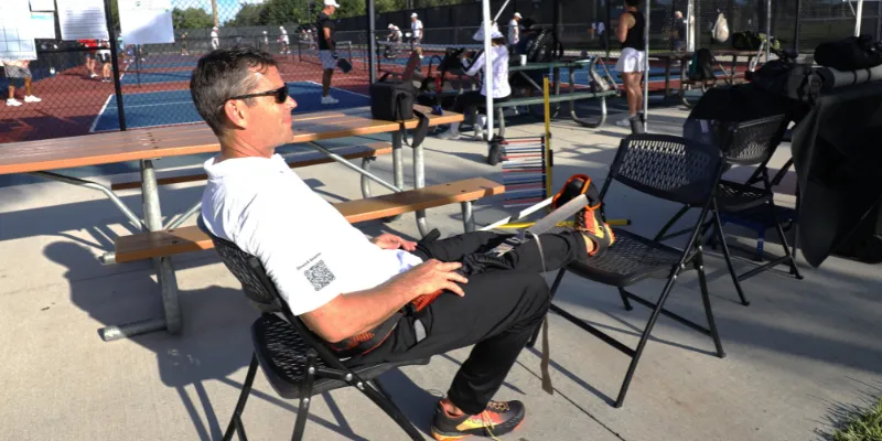 Pickleball player seated outdoors using BFX Stretch with one leg extended before play.